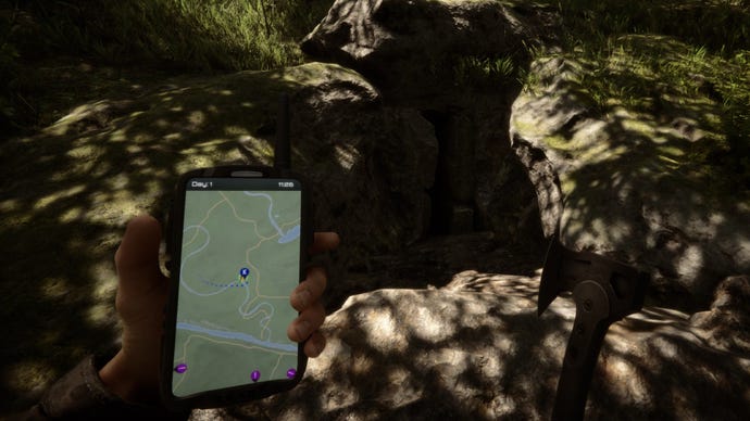 A player stands by a cave while holding their GPS in Sons Of The Forest.